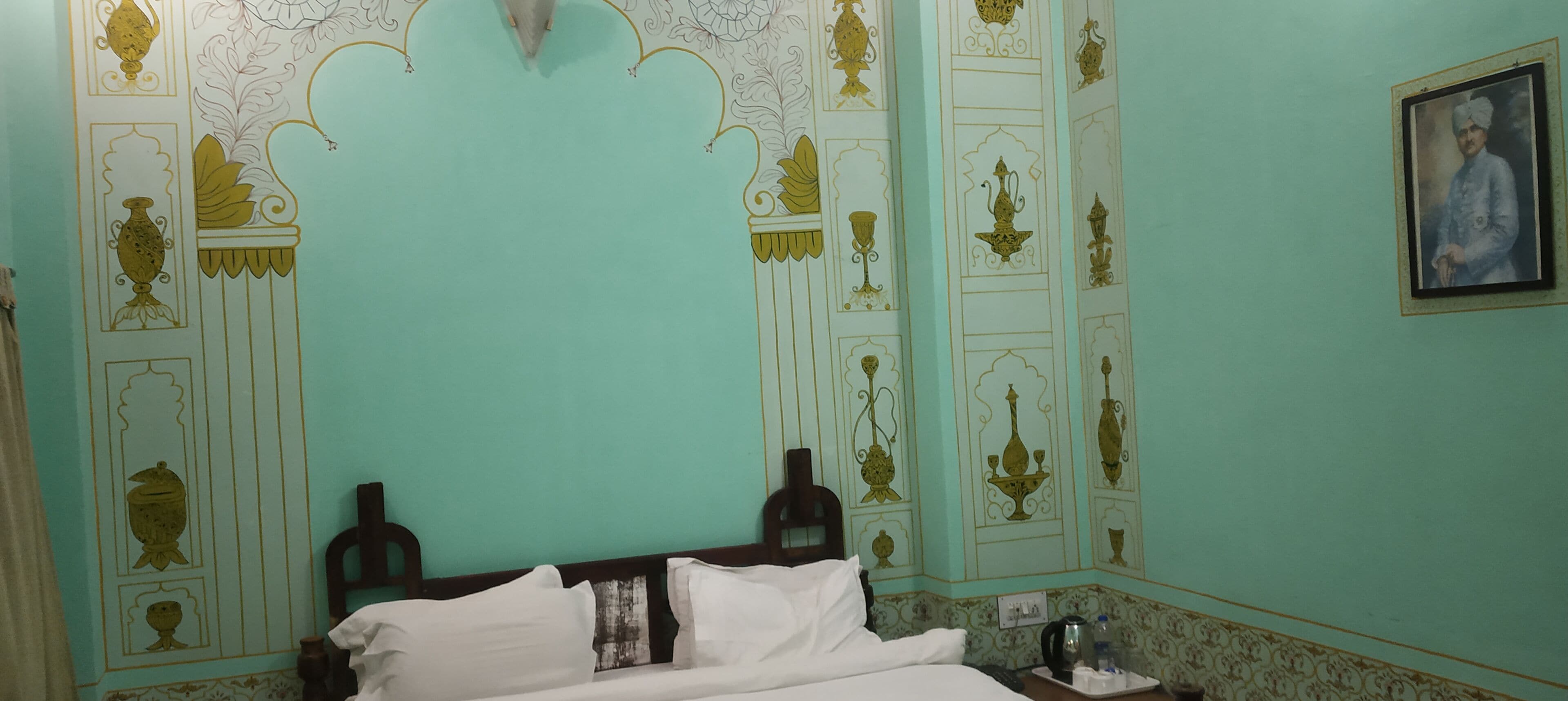 A room with a bed, a nightstand, a framed picture on the wall, and decorative wall patterns.