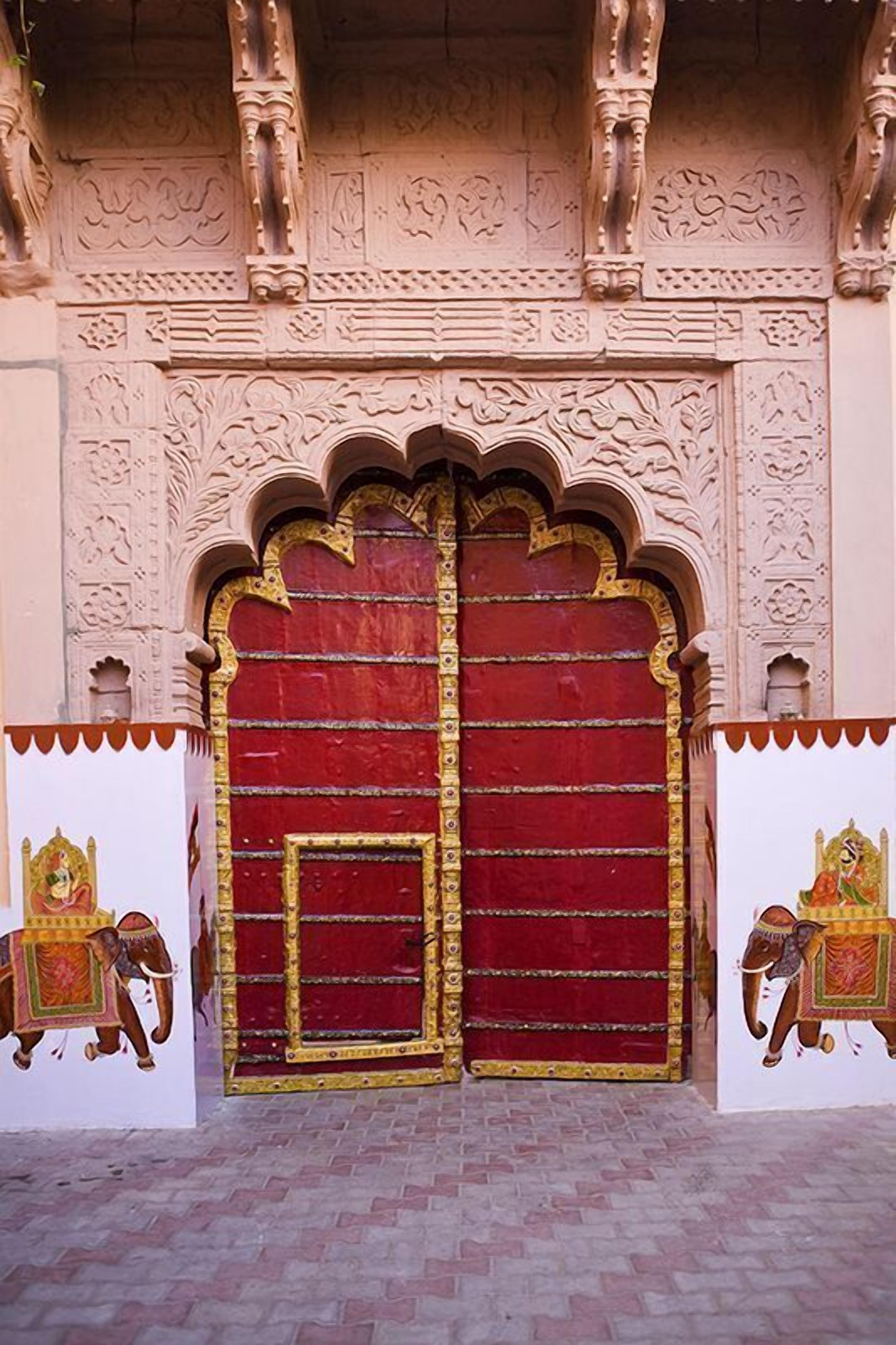 A red door with intricate carvings and a small balcony with a railing.