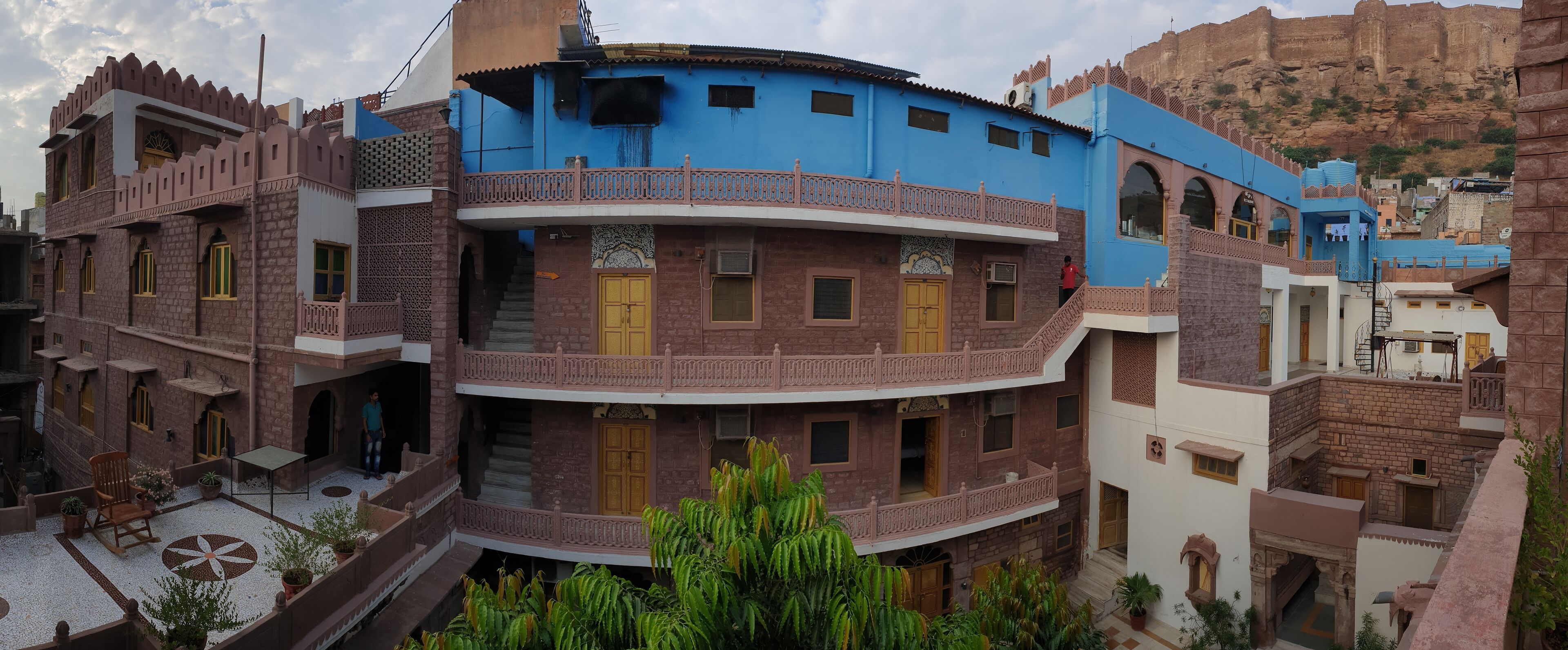 A multi-story building with traditional architecture, featuring balconies and a courtyard with potted plants.