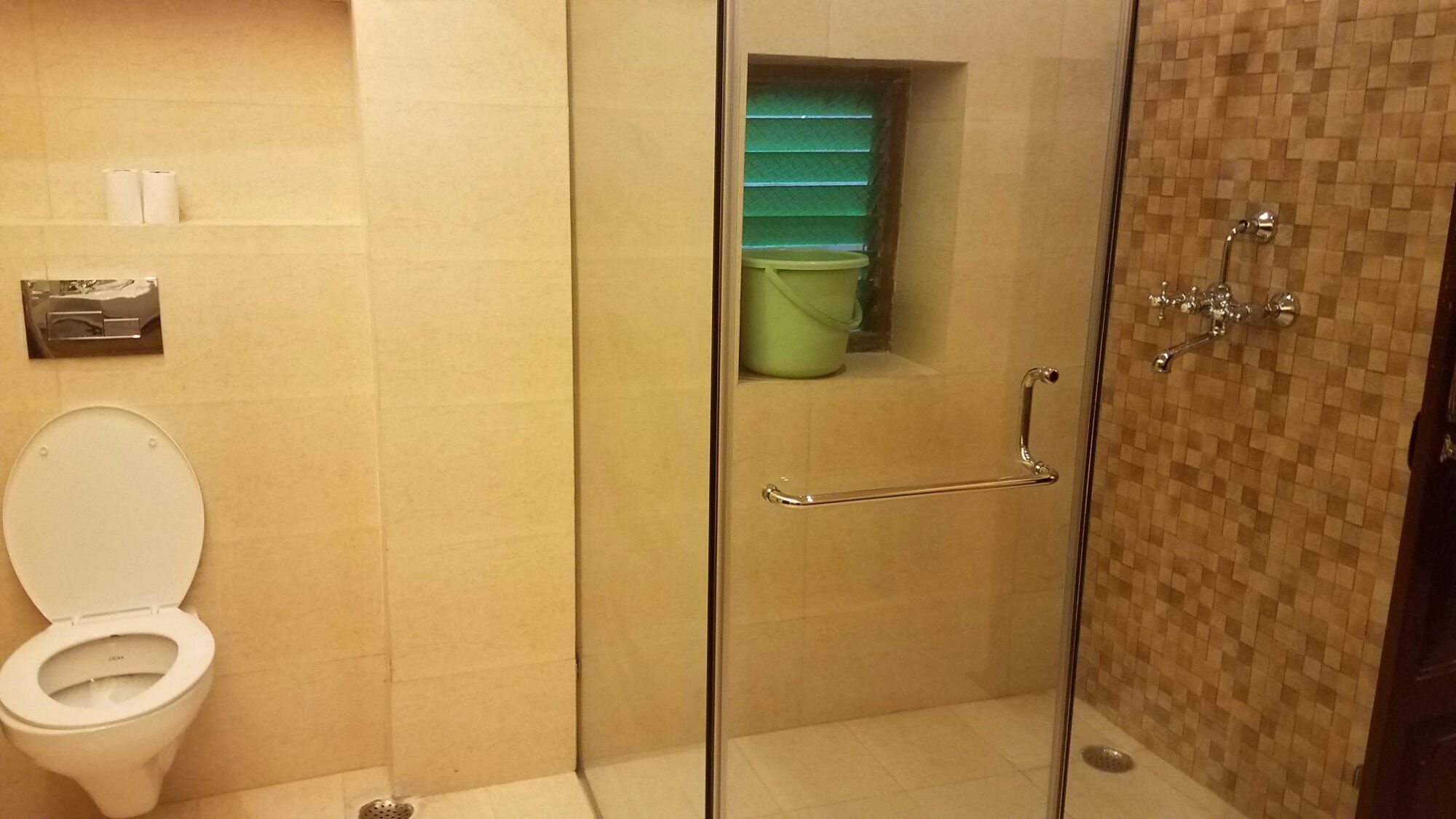 Ein Badezimmer mit Duschkabine aus Glas, einer weißen Toilette und einem grünen Mülleimer.