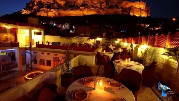 A rooftop restaurant with tables set for dining, overlooking a historic fort. - Krishna Prakash Heritage Haveli (Jodhpur)