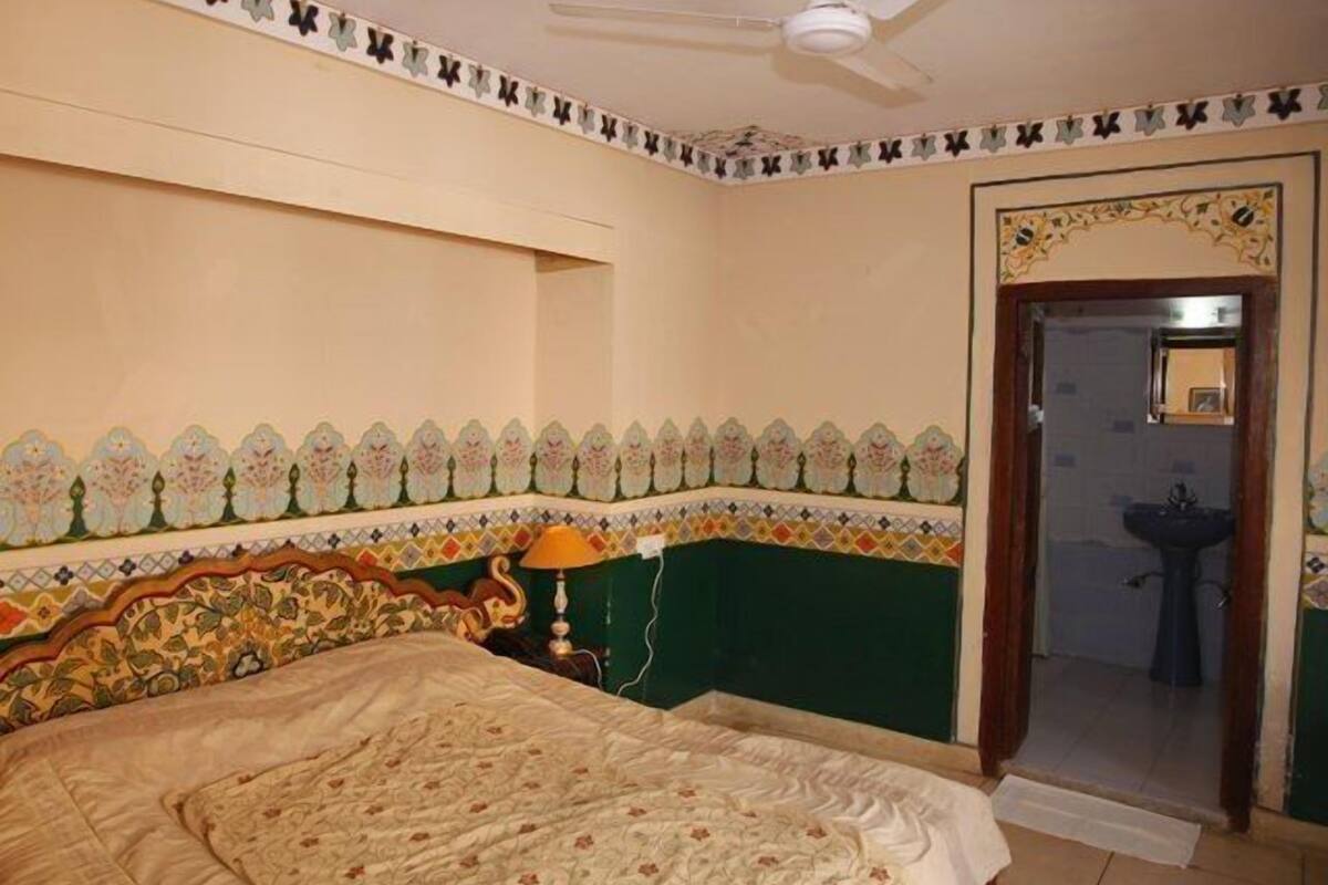 Een slaapkamer met een bed, een nachtkastje, een lamp en een deur naar een badkamer.