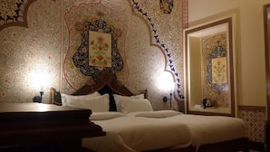 A hotel room with a large bed, a wooden headboard, and ornate wall decorations. - Krishna Prakash Heritage Haveli (Jodhpur)