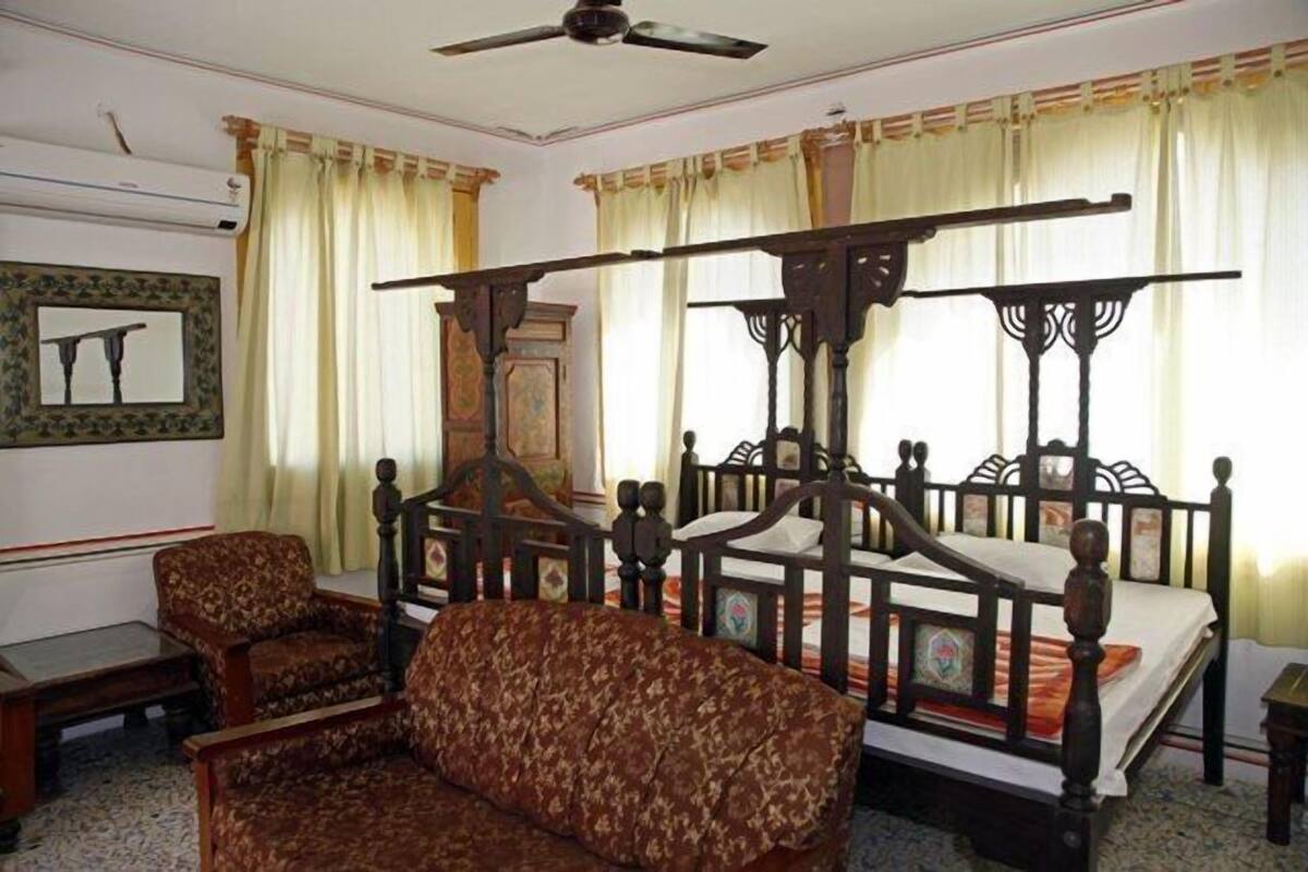 Een kamer met een hemelbed, twee gestoffeerde fauteuils, een bijzettafeltje en een plafondventilator.