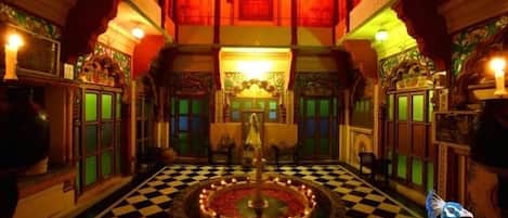 A traditional interior with a checkered floor, a central fountain, and ornate wooden balconies.