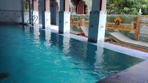 A swimming pool with clear blue water, tiled walls with dolphin patterns, and a tiled deck area with lounge chairs. - Krishna Prakash Heritage Haveli (Jodhpur)