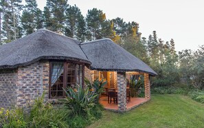 Una casa rústica con techo de paja, muros de ladrillo y un pequeño patio con mesa y sillas.