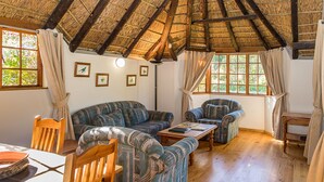 Un salon chaleureux avec un toit de chaume, des meubles en bois et de grandes fenêtres ornées de rideaux.