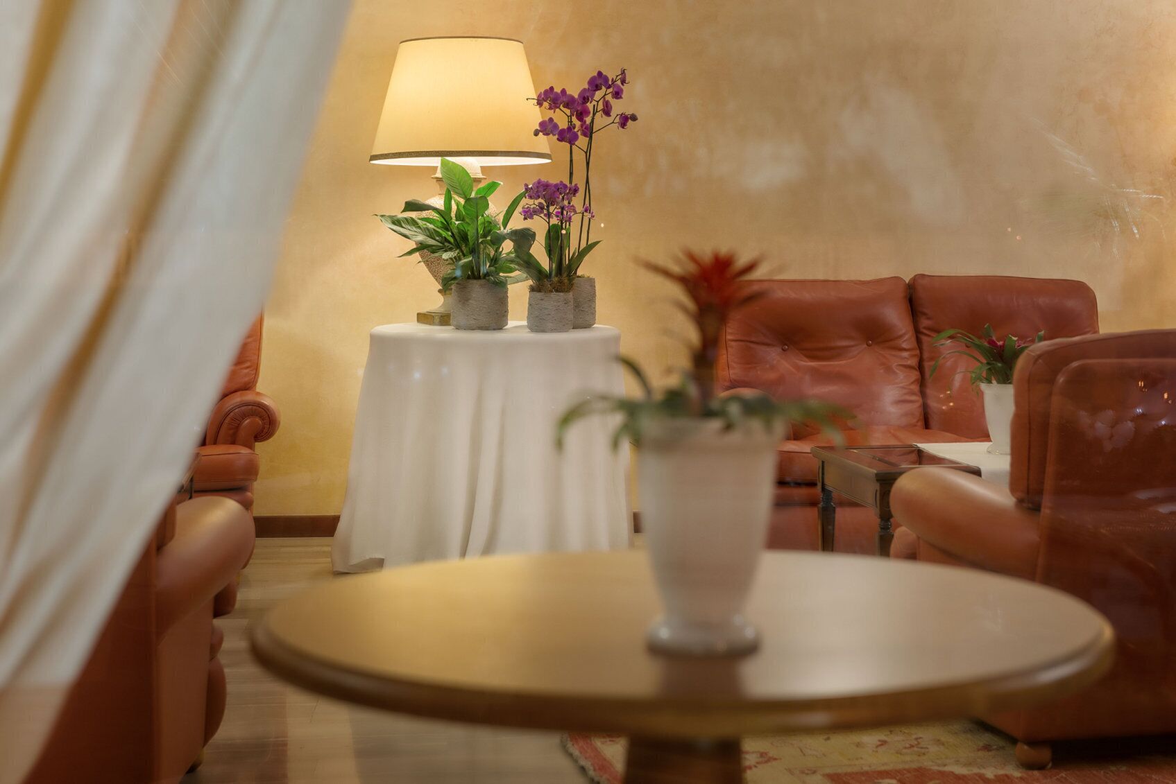 A cozy room with a leather sofa, a small round table, and a lamp. There are potted plants on a side table.