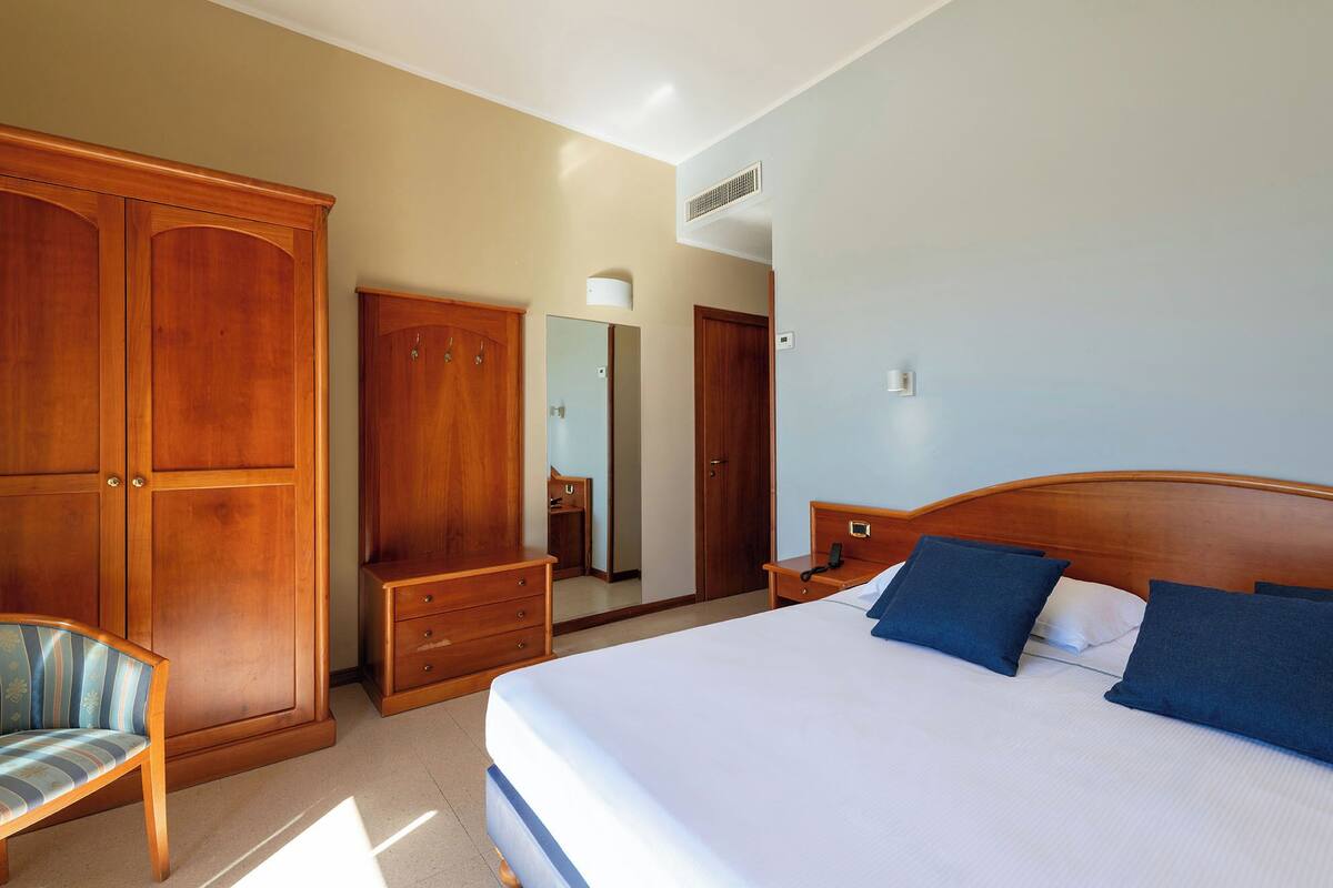 Quarto com cama grande, guarda-roupa de madeira, penteadeira e uma cadeira.