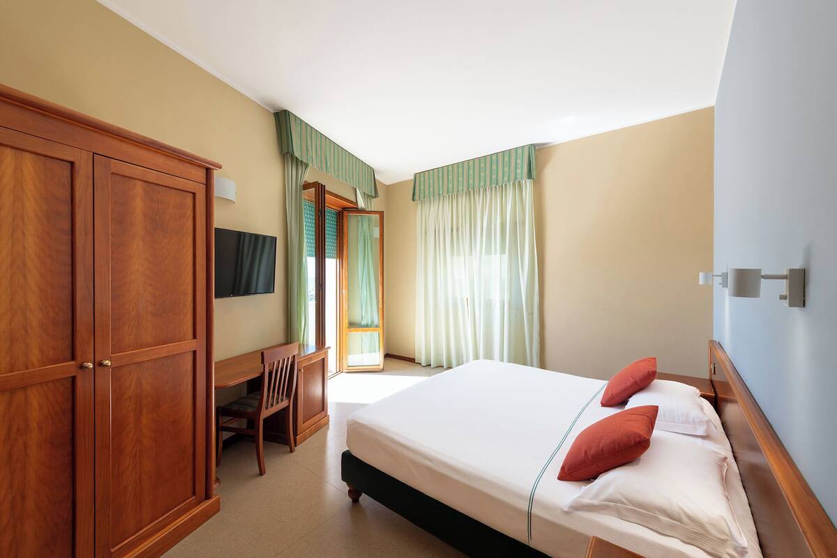 Quarto de hotel com cama, escrivaninha e guarda-roupa.