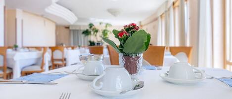 Una mesa de comedor dispuesta con vajilla blanca, una servilleta azul y una planta en maceta con flores rojas.