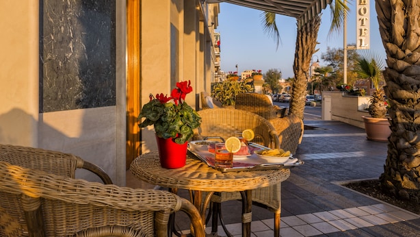Een hotelterras met rieten meubels, een tafel met een dienblad eten en drinken, en een bord met de naam van het hotel.