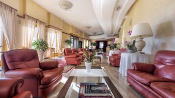Eine großzügige Hotelhalle mit Ledersofas, einem Couchtisch mit Büchern und Zimmerpflanzen.
