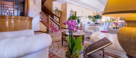 A spacious living area with a staircase, white sofas, a coffee table, and potted plants.
