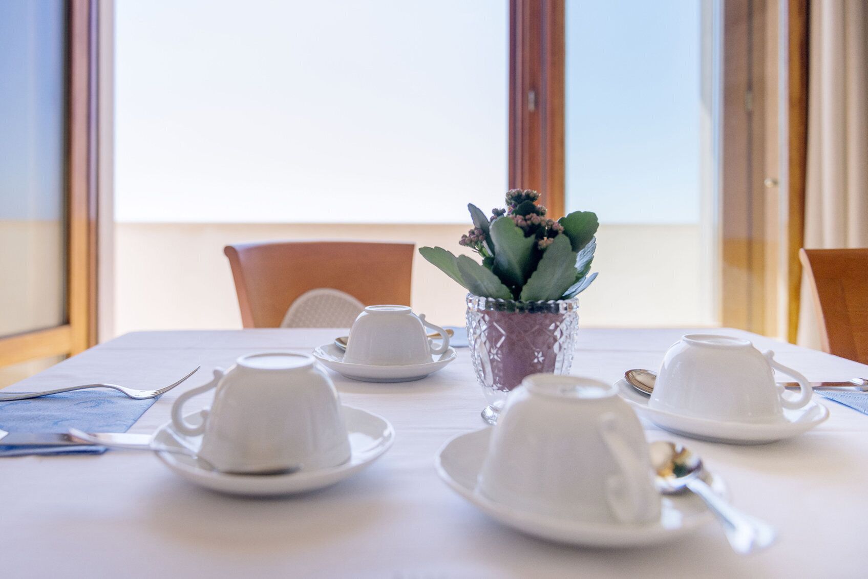 Une table à manger dressée avec de la vaisselle blanche et une plante en pot.