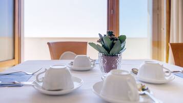 A dining table set with white dishes and a potted plant.