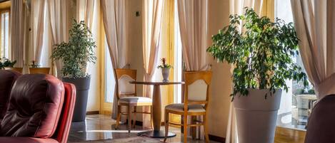 A hotel lobby with leather sofas, a round table, two chairs, and large potted plants.