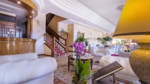 Een ruime lobby met een statige trap, comfortabele zithoek en decoratieve planten.