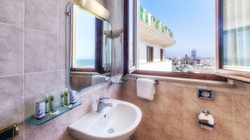 A bathroom with a sink, mirror, and toiletries on a shelf. A window offers a view of a cityscape.
