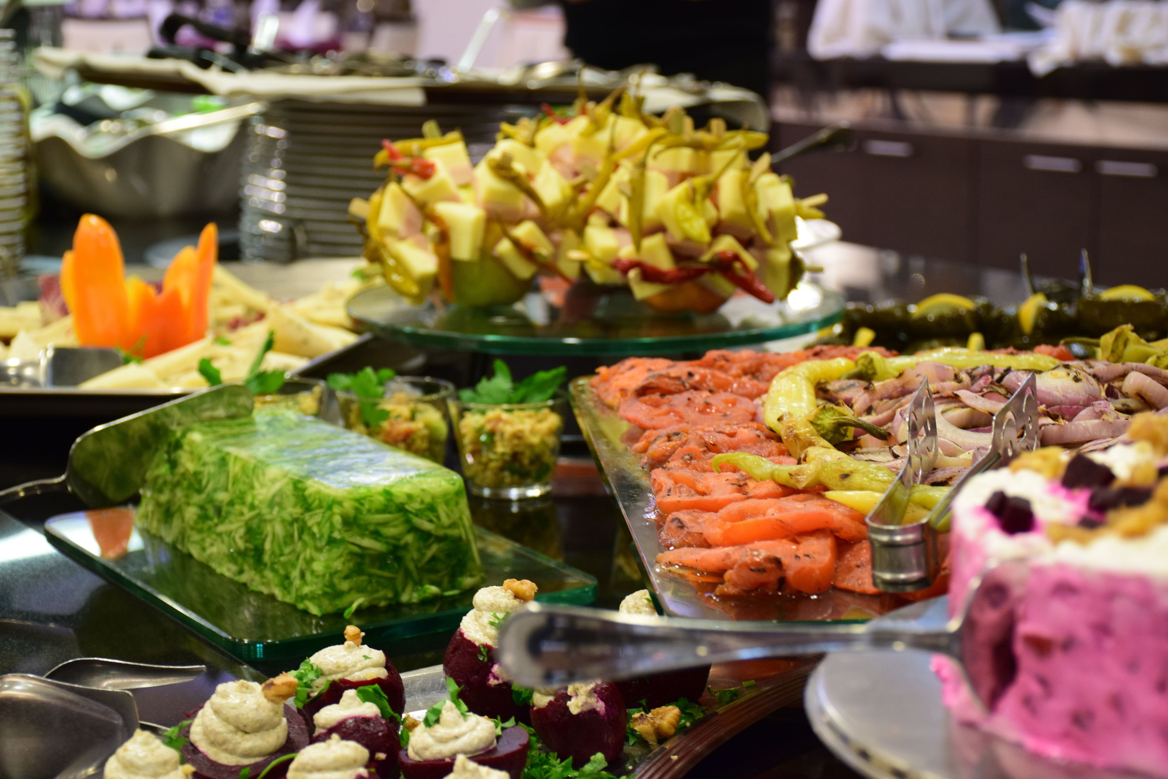 A buffet with various food items including a green vegetable dish, a tray with sliced vegetables, and a dessert.