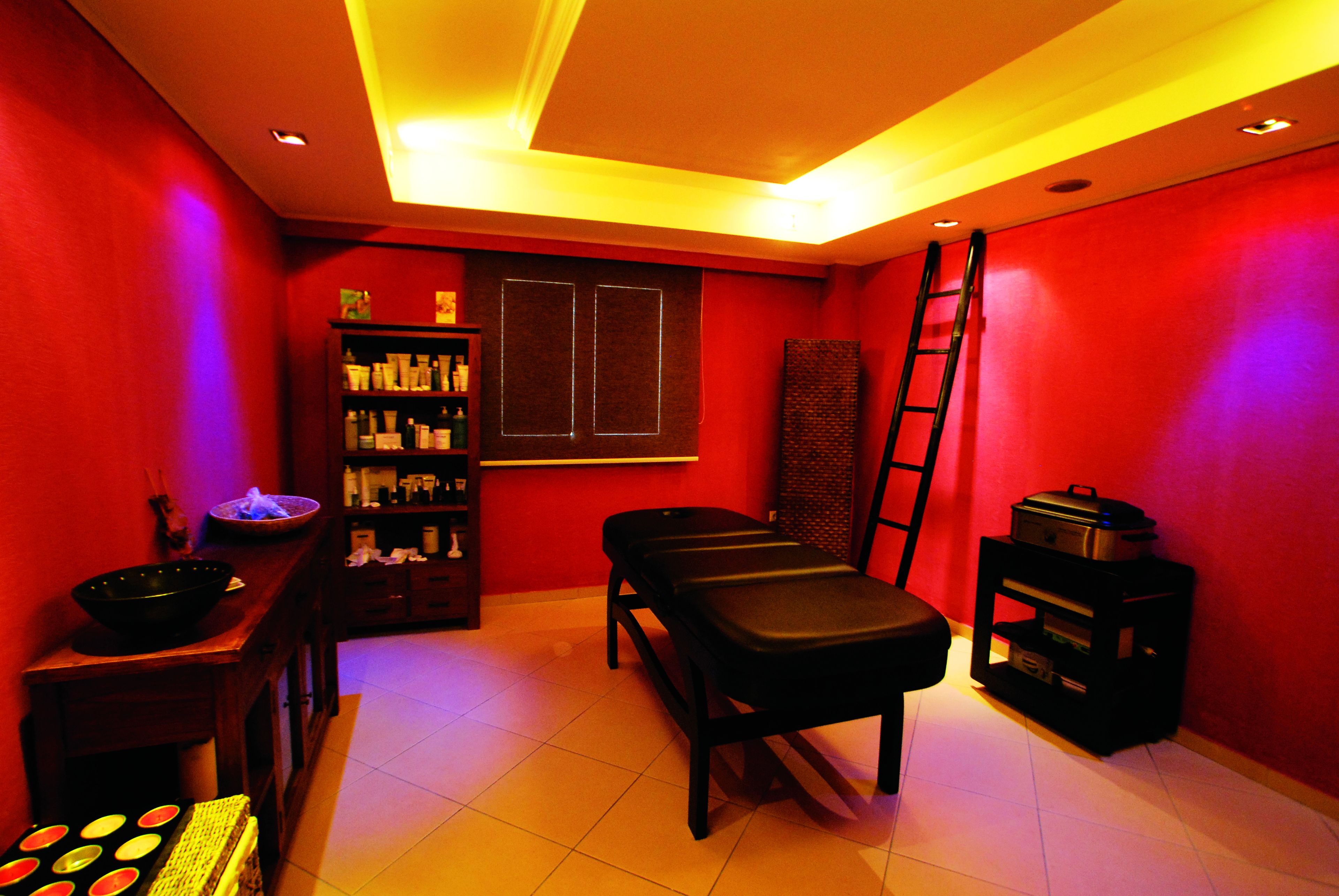 A room with a massage table, a bookshelf, a ladder, and a shelf with various items.