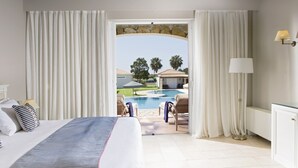 A hotel room with a bed, a view of a swimming pool, and a stone archway. - Olympia Golden Beach & Spa (Andravida-Kyllini)