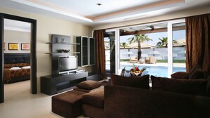 A modern living room with a sectional sofa, a flat-screen TV, and a dining area with a pool view. - Olympia Golden Beach & Spa (Andravida-Kyllini)