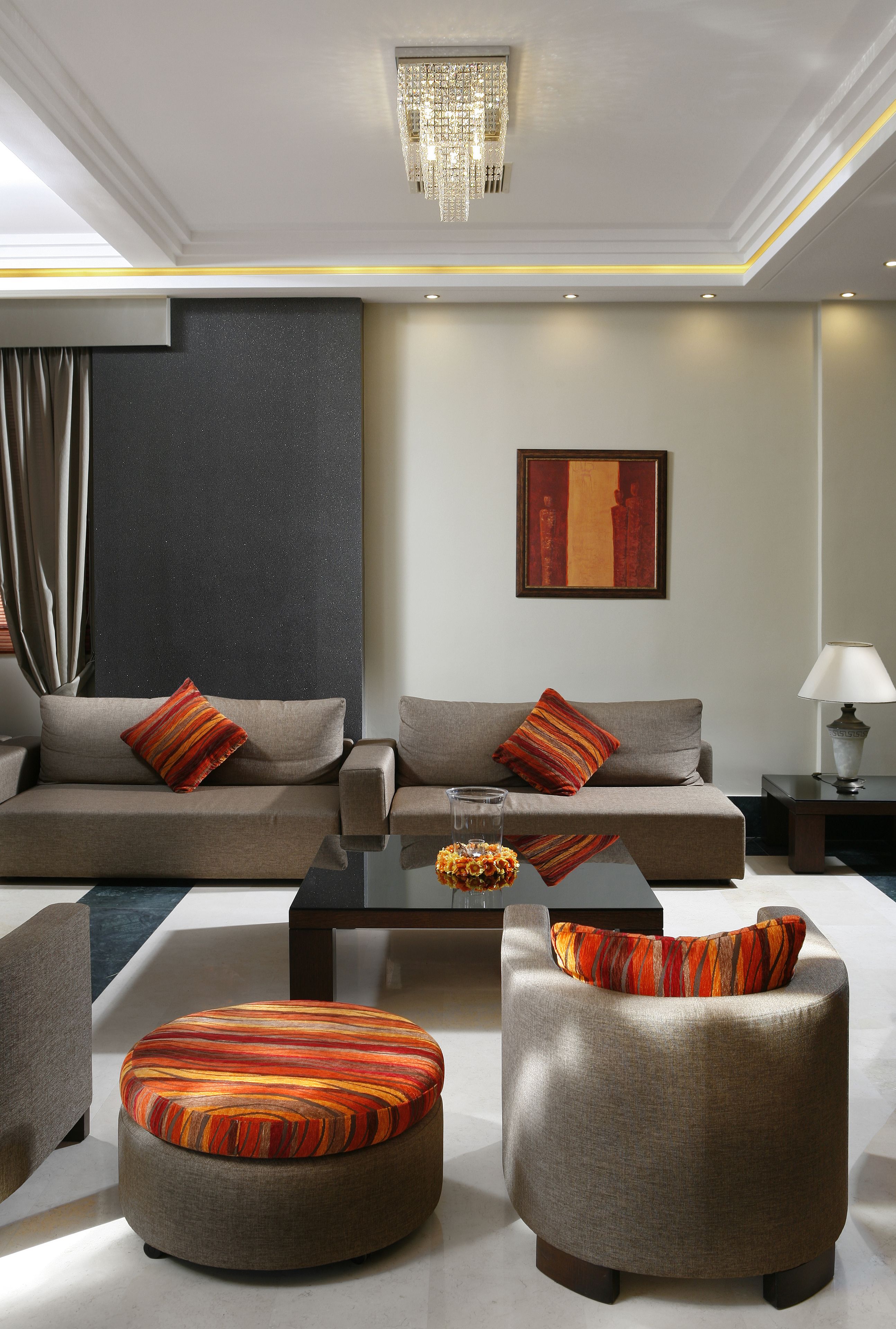 A modern living room with a sofa, ottoman, and coffee table, featuring a chandelier and artwork on the wall.