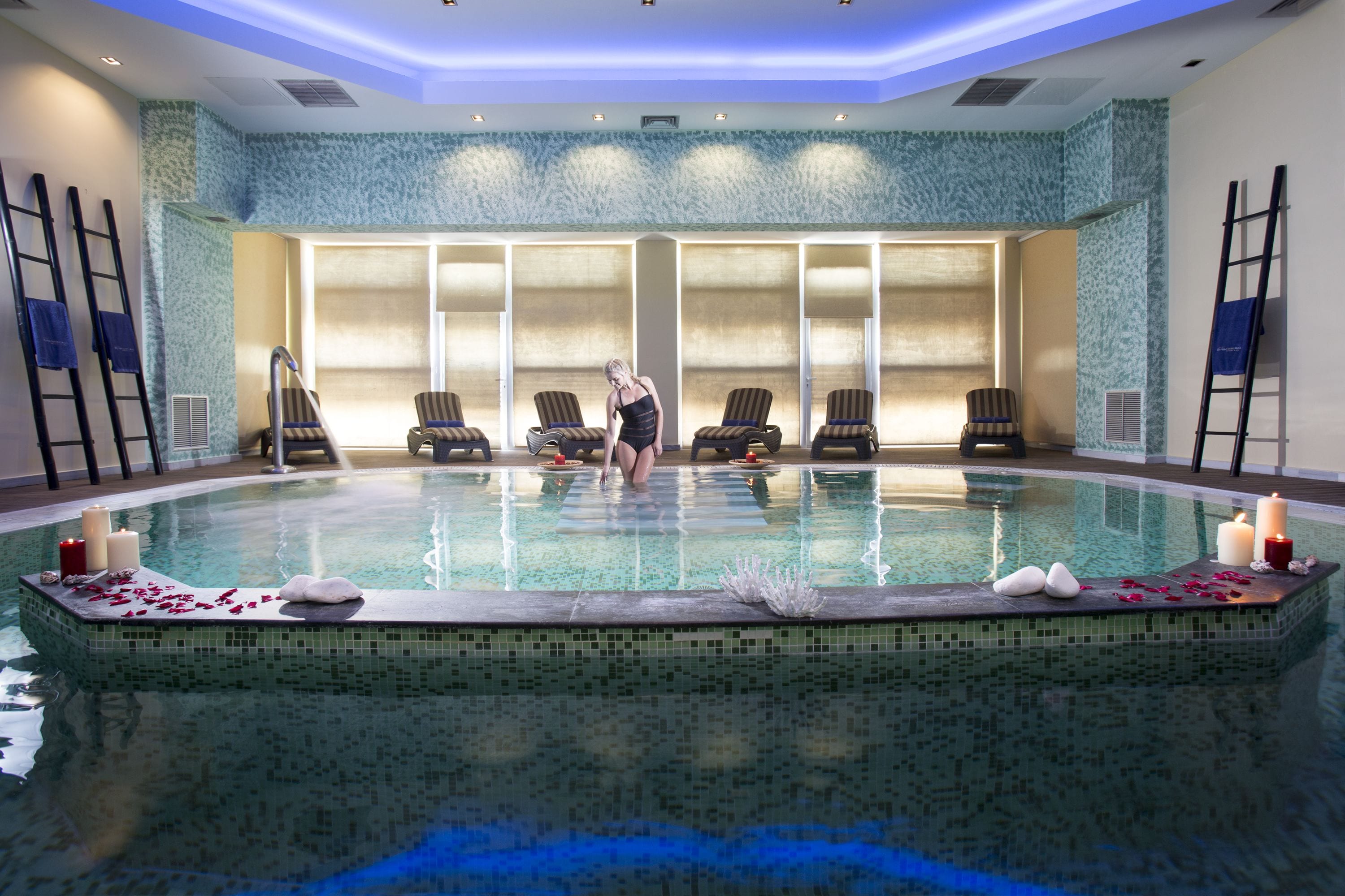 A swimming pool with a tiled interior, lounge chairs, and candles.