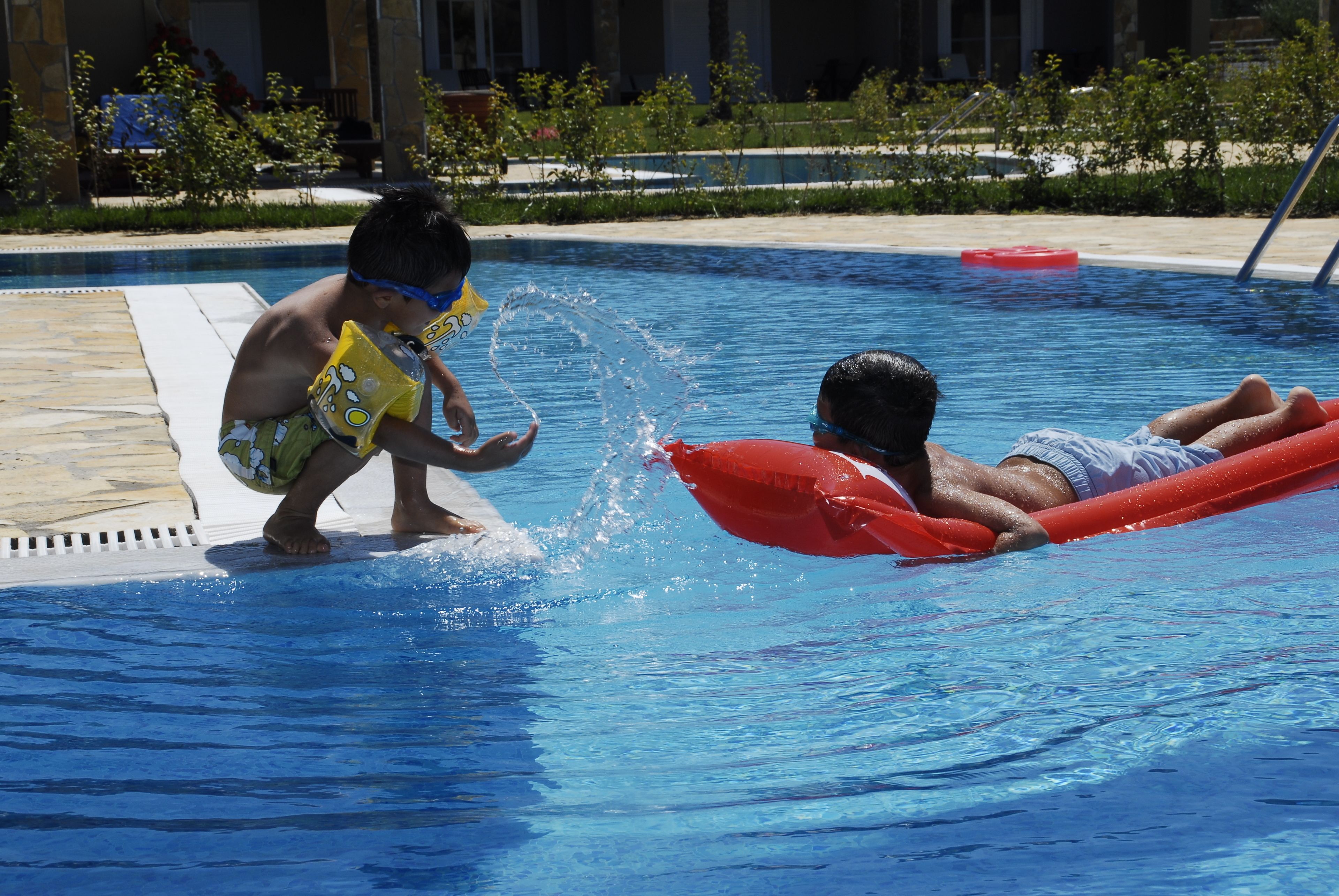 Een zwembad met twee kinderen die aan het spelen zijn, één op een rode luchtbed en de ander in het water.
