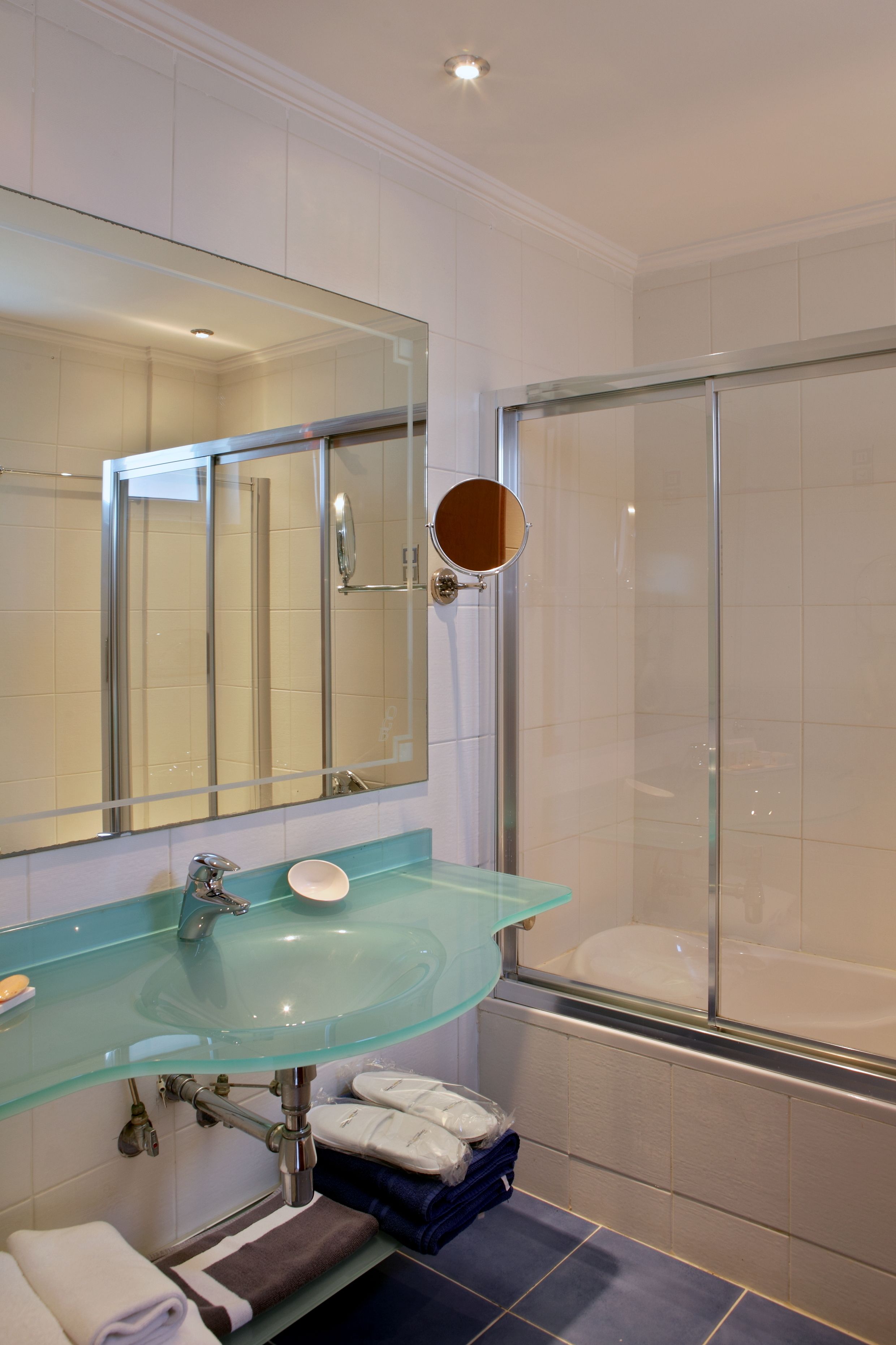A bathroom with a glass sink, a large mirror, a shower, and a towel rack.