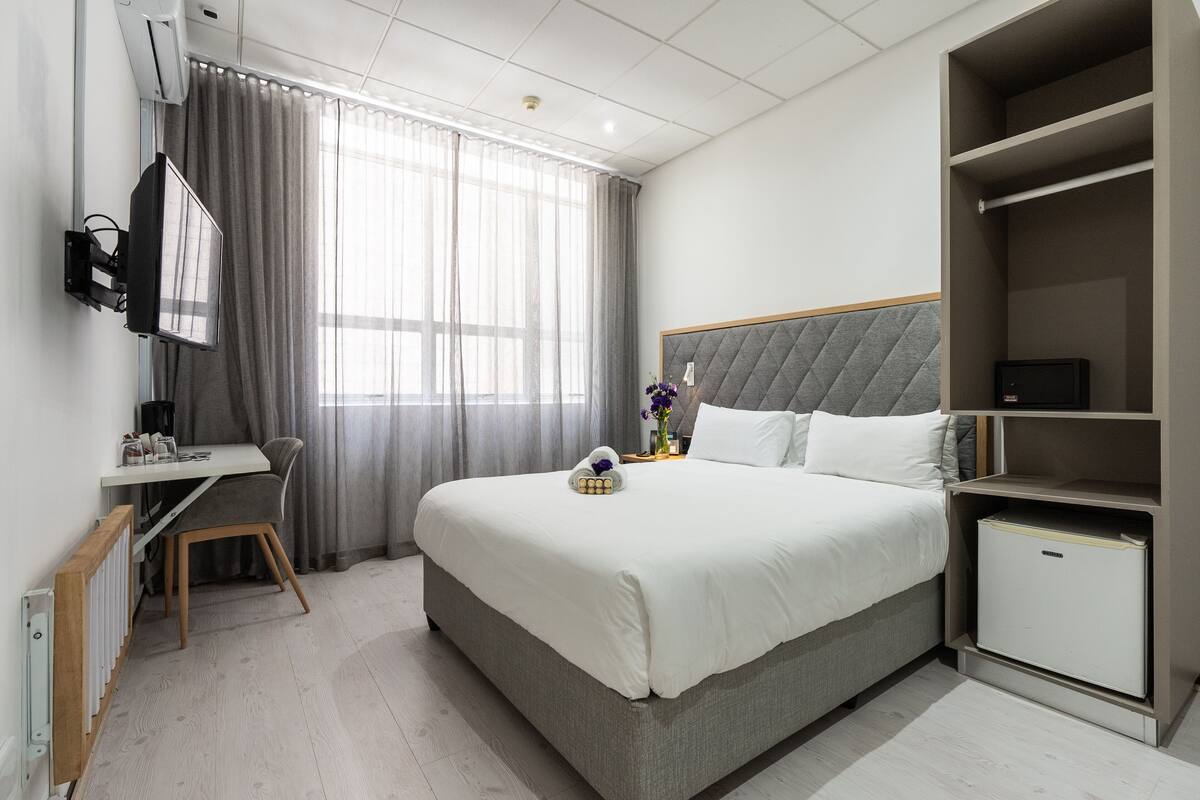 Ein Hotelzimmer mit Bett, Schreibtisch, Stuhl, Kleiderschrank und kleinem Kühlschrank.