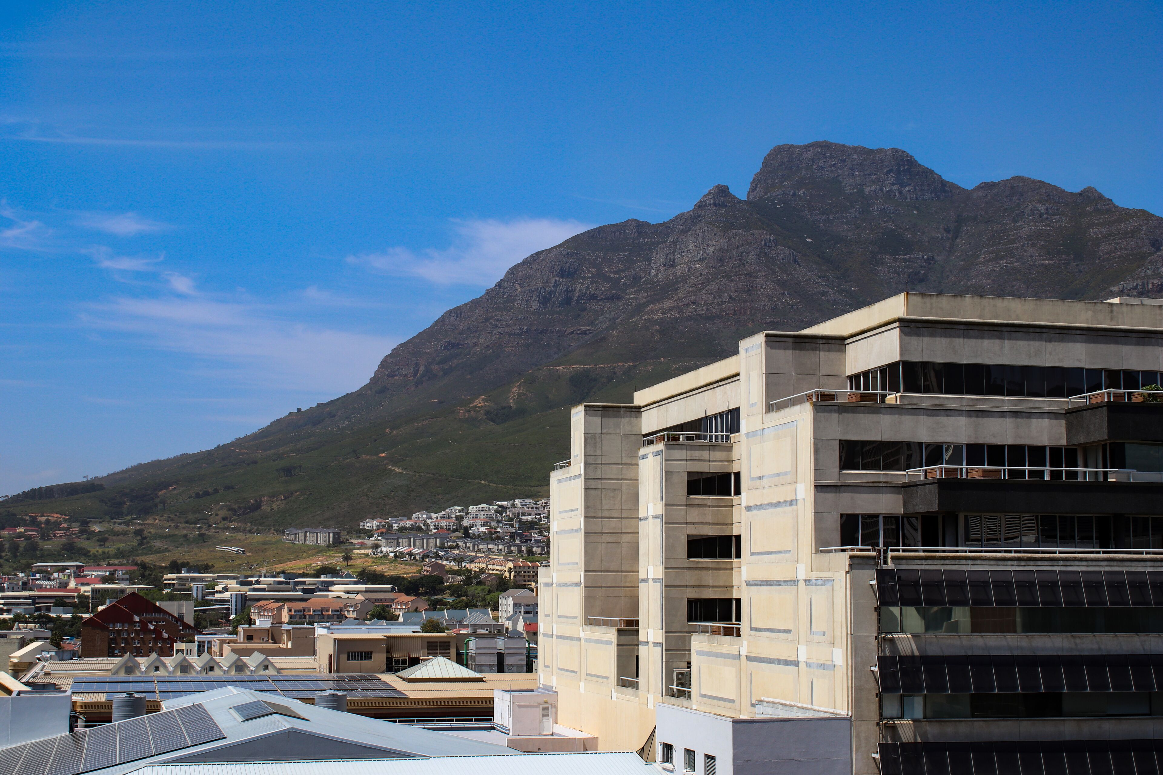 Un bâtiment moderne à étages multiples, doté de grandes fenêtres, situé dans un paysage urbain avec une montagne en arrière-plan.