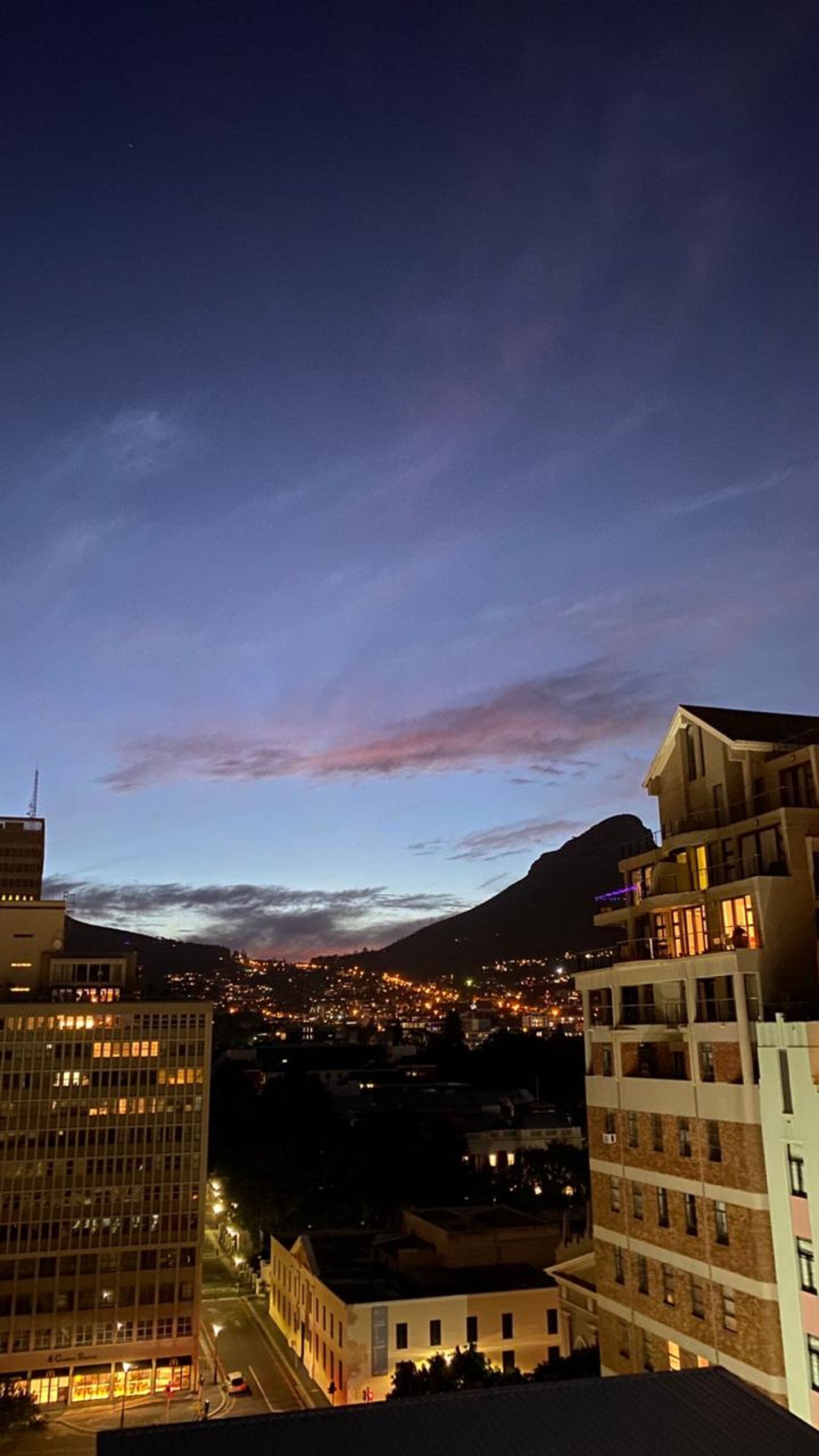 A cityscape at dusk with a mountain in the background.