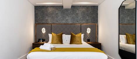 Una habitación de hotel moderna con una cama grande, cabecera con iluminación integrada, un espejo y suelo de madera.
