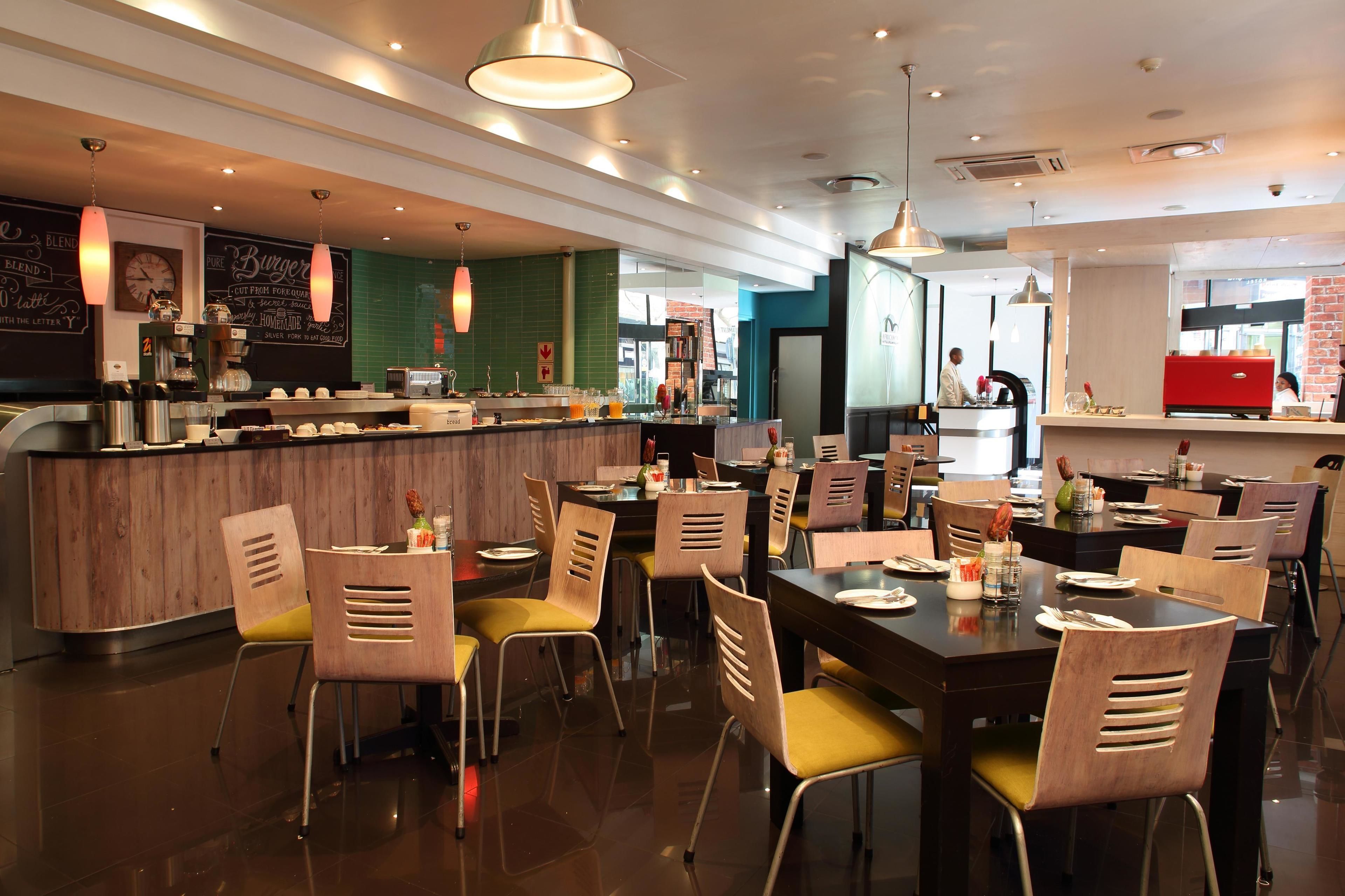 A modern restaurant interior with wooden tables and chairs, a bar area, and a visible counter.
