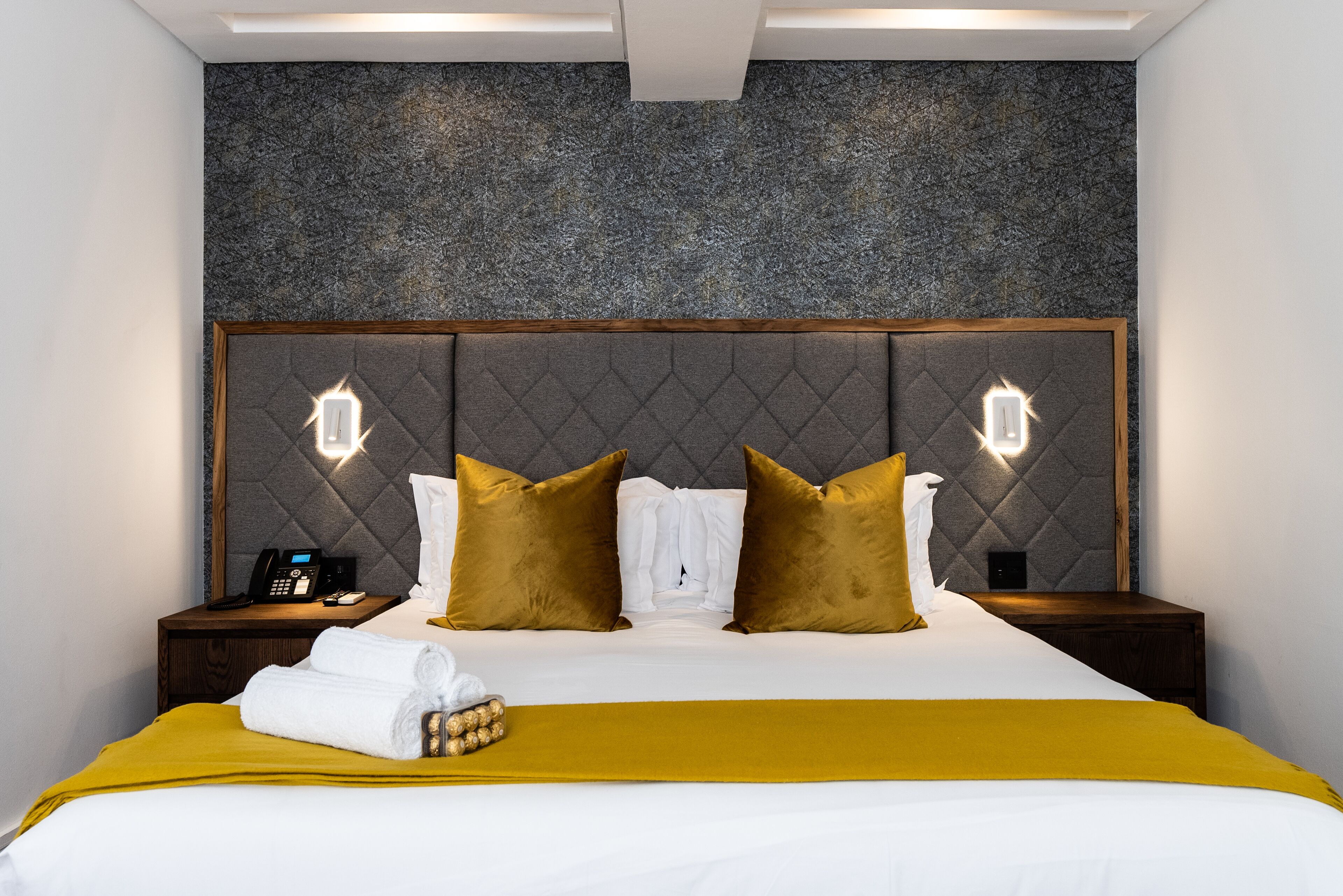 A hotel room with a bed, a nightstand, a telephone, and a wall with a textured pattern.