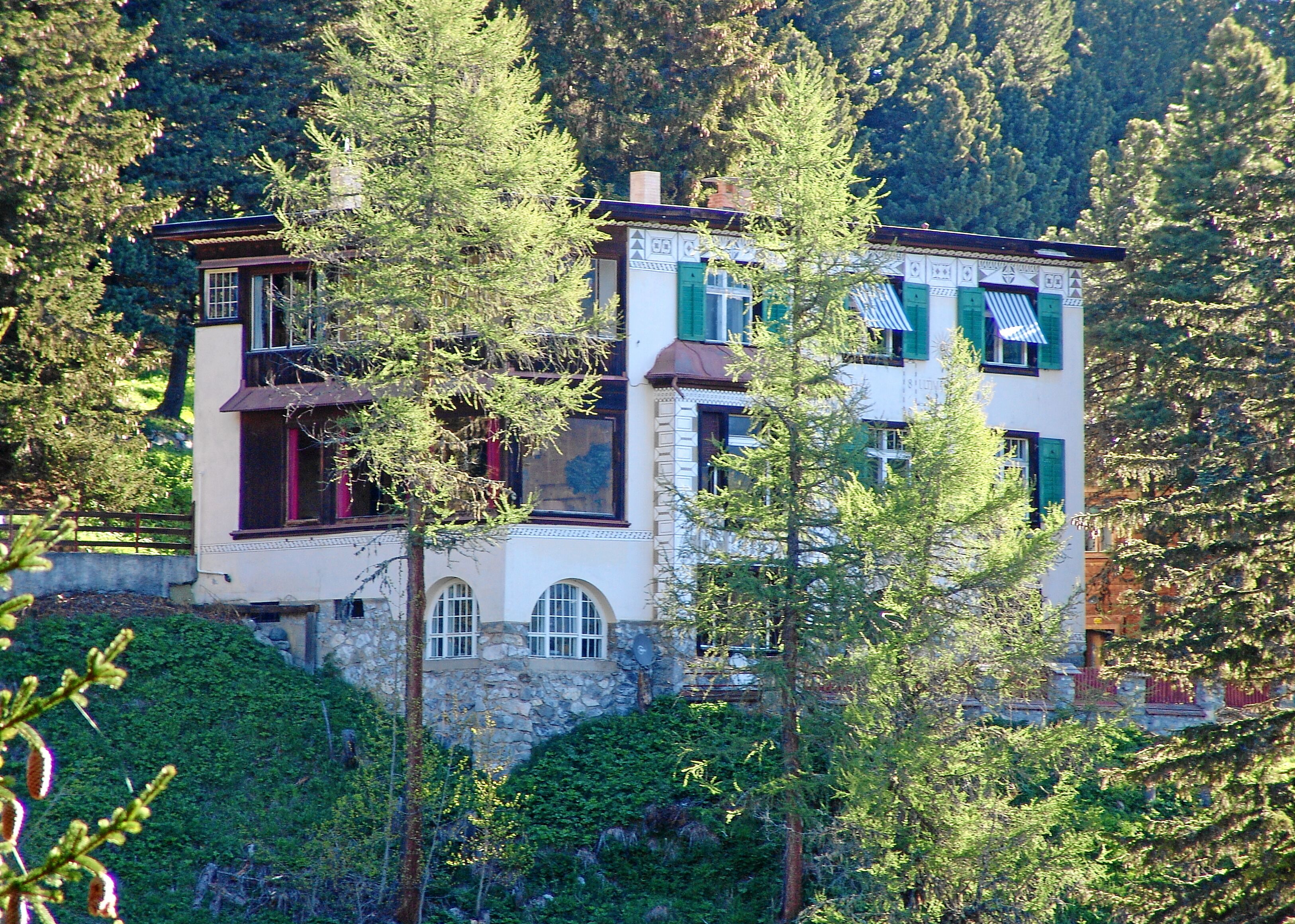 Un immeuble à plusieurs étages, doté d’une façade en pierre, de volets verts et d’un balcon.