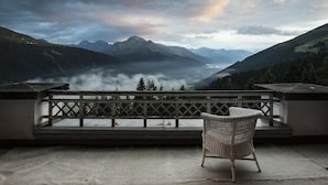 A balcony with a wicker chair overlooking a mountainous landscape with a valley and mist. - Schatzalp Snow & Mountain Resort (Davos)