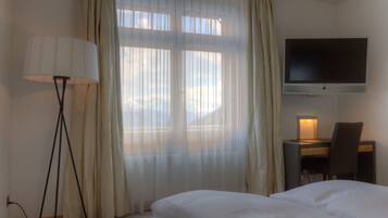 Une chambre d’hôtel comprenant un lit, un bureau avec une chaise, un téléviseur fixé au mur et une lampe sur pied.