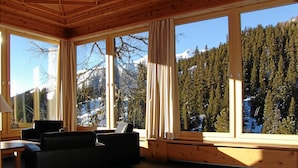 A cozy room with large windows, wooden ceiling, and a view of snow-capped mountains and dense forest. - Schatzalp Snow & Mountain Resort (Davos)