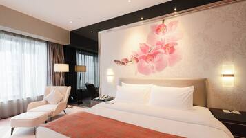 A hotel room with a large bed, a chair, a desk with a phone, and a wall with a floral design.