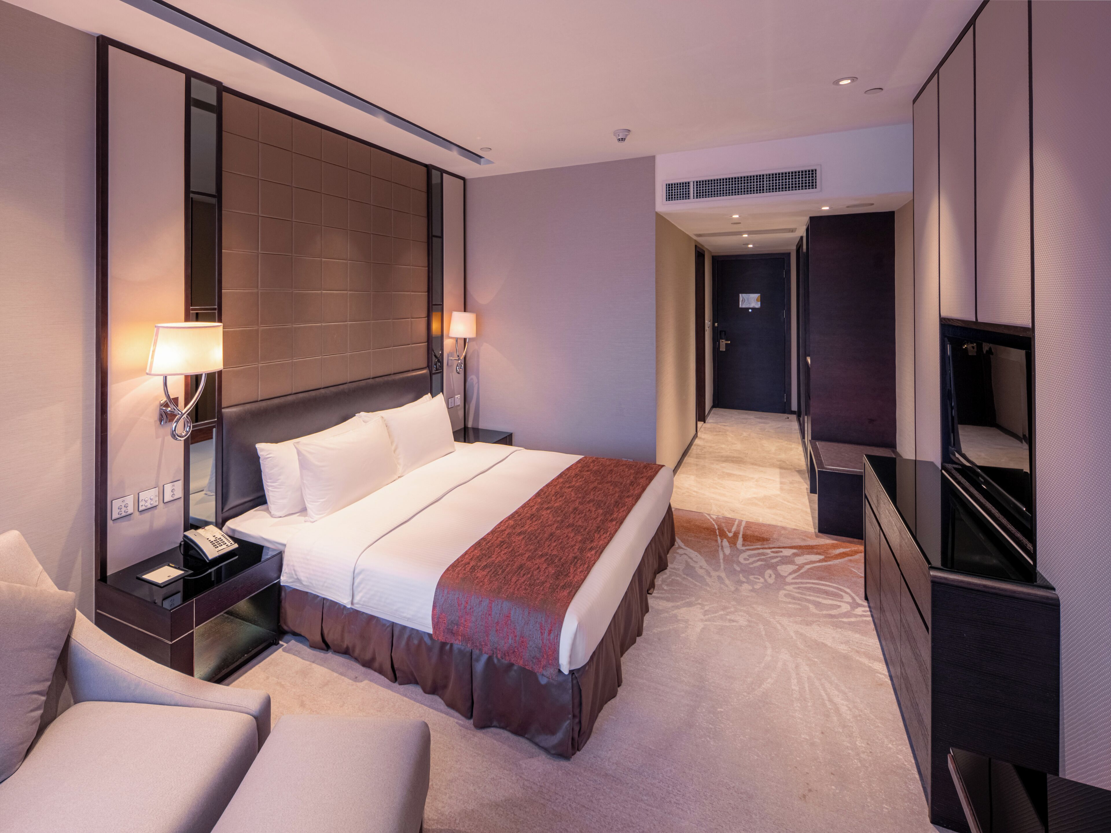 A hotel room with a large bed, bedside tables, a desk, a chair, a TV, and a walk-in closet.