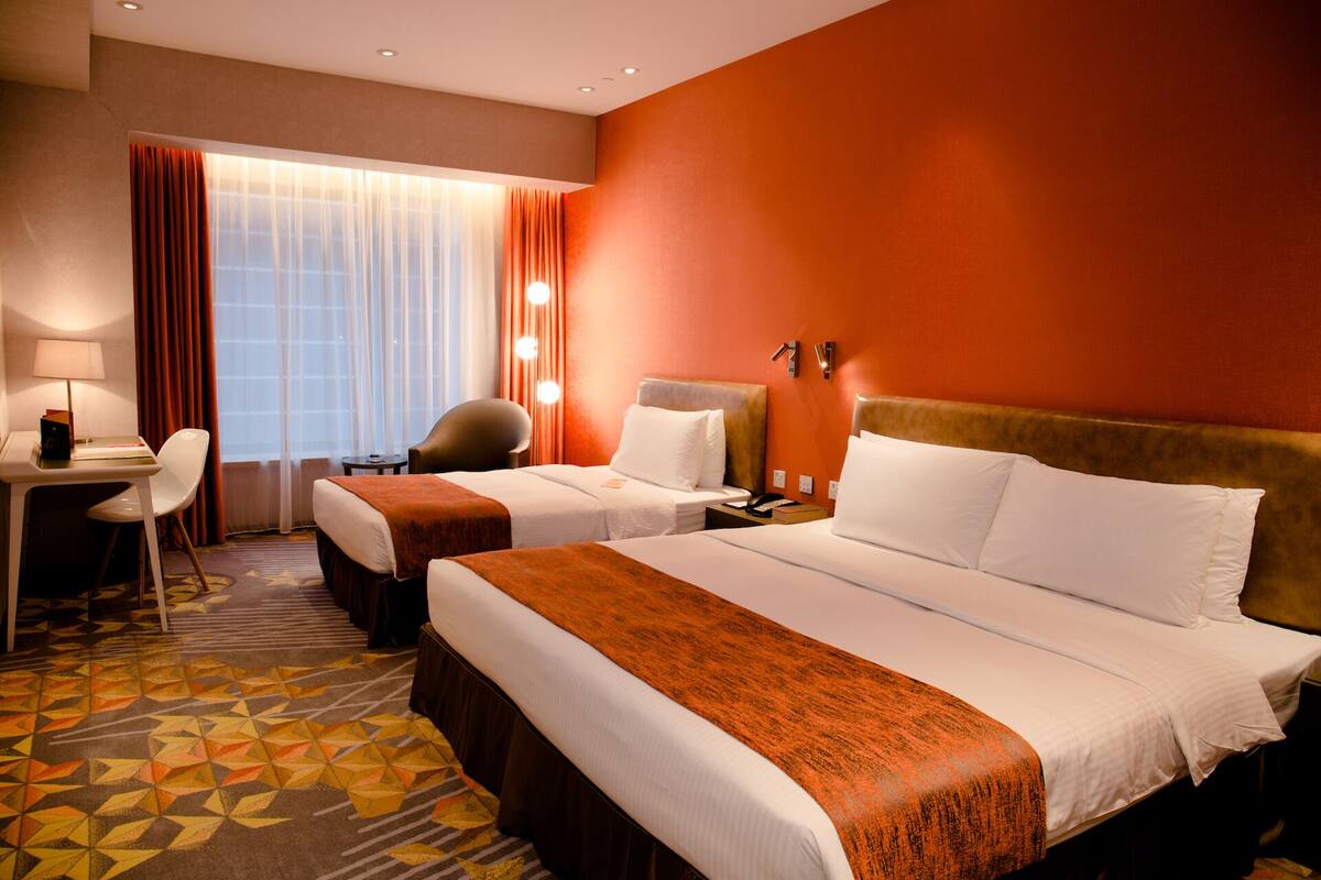 A hotel room with two beds, a desk, a chair, and a large window with curtains.