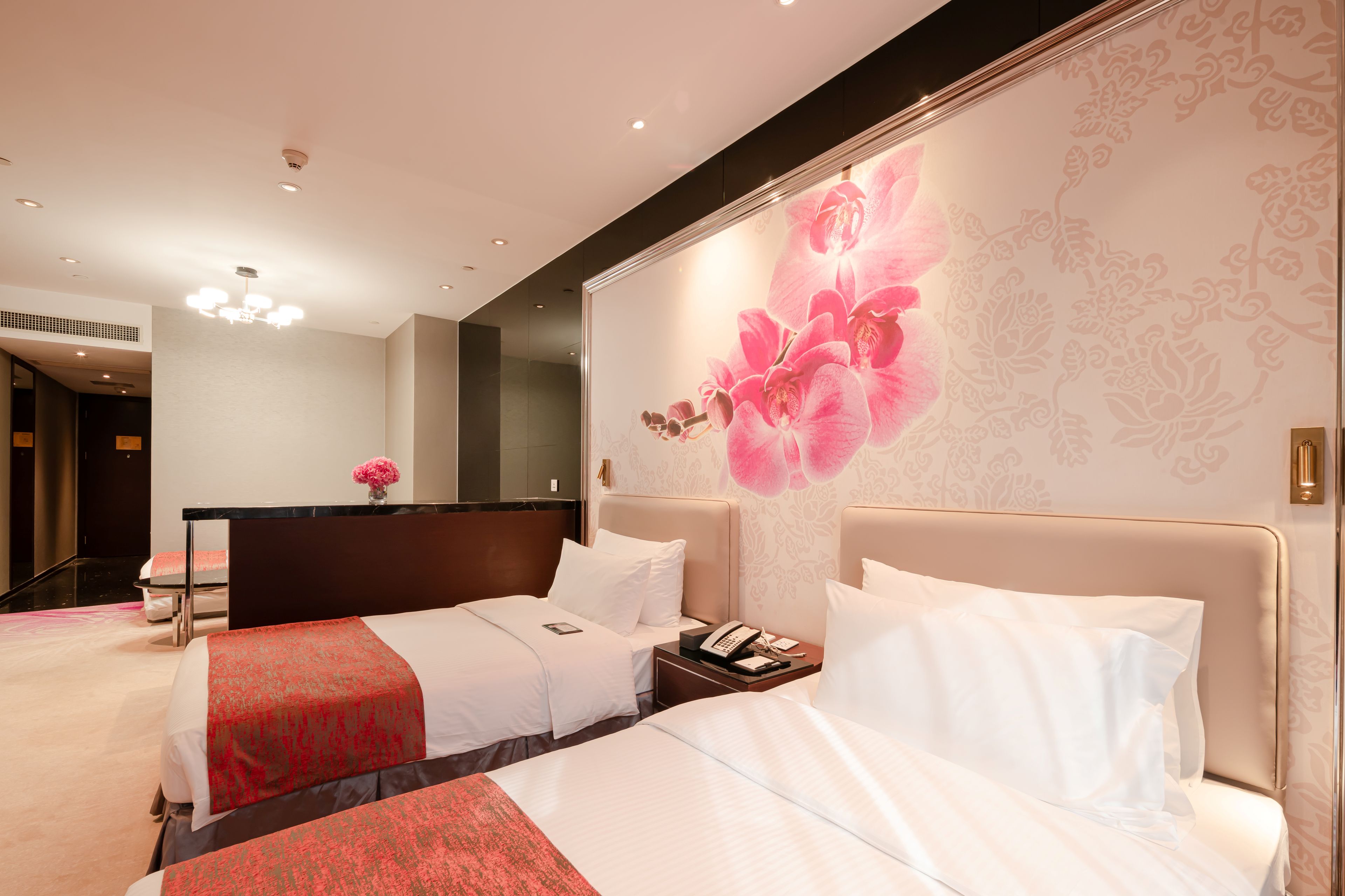 A hotel room with two beds, a desk, and a large floral wall mural.