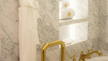 A bathroom with a marble floor, a white robe hanging on a rack, a gold faucet, and a mirror with shelves.