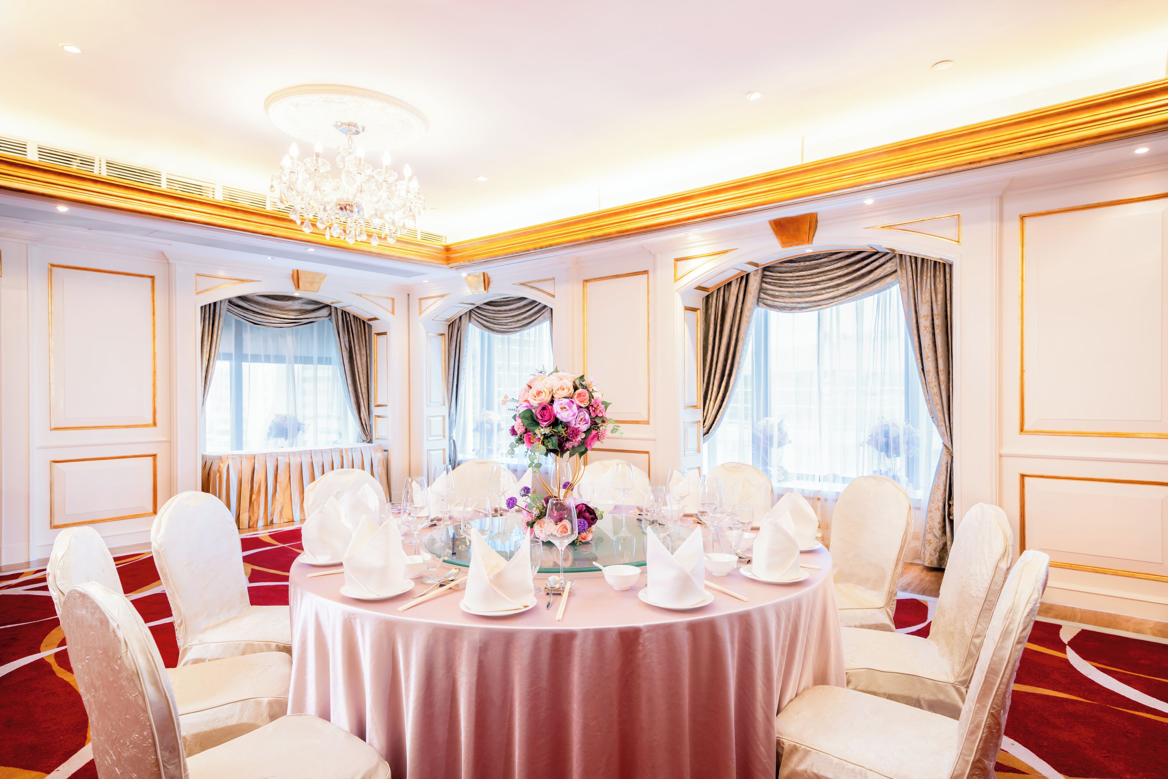 Un comedor formal con mesas redondas, sillas blancas y una araña.