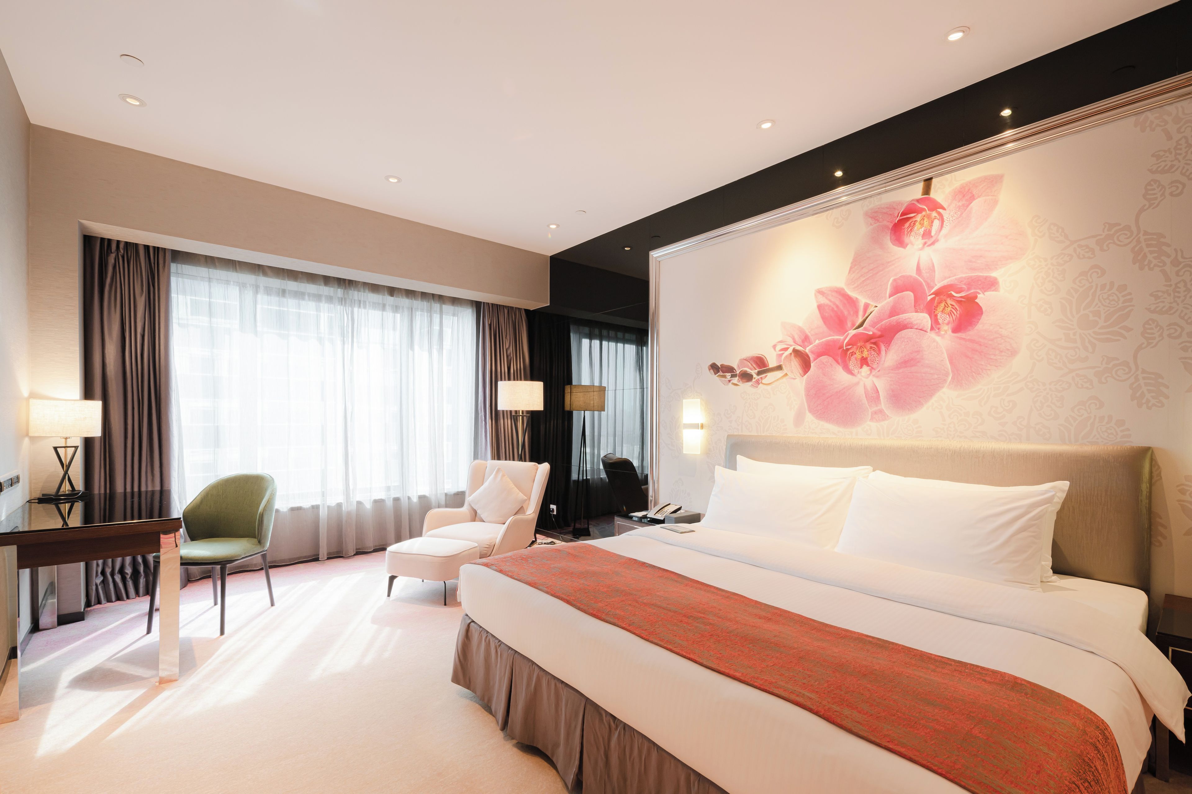 Une chambre d’hôtel avec un grand lit, deux fauteuils, un bureau et un grand décor mural représentant des motifs floraux.
