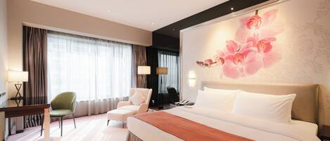 A hotel room with a large bed, two chairs, a desk, and a large floral wall mural.